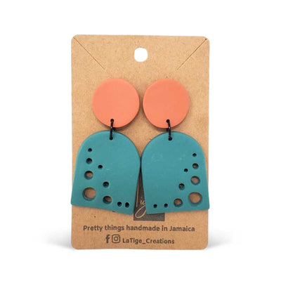 Handmade earrings with orange circles and teal arches with cutouts, displayed on a card reading "Pretty things handmade in Jamaica."